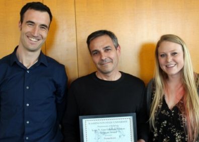 Tom Rotolo, standing in the center, receives the Louis N. Gray Student Advocate Award from Adam Roth, standing to the left, and Sadie Ridgeway standing to the right, all three are smiling at the camera.
