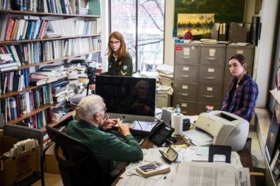 WSU Journalism students Rebecca White (in a plaid shirt) and Shannon Heckt (holding a video camera) interview Professor Jim Short in his office in Wilson-Short Hall.