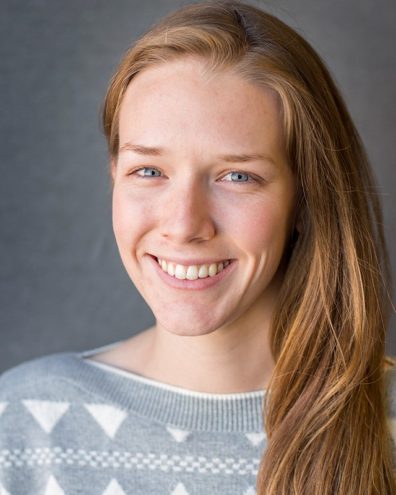 A front facing photo of Alana Inlow, from the shoulders up. They are looking into the camera and smiling.