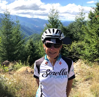 Front facing photo of Amy Wharton, standing on a mountain-top in Oregon, wearing a helmet and bicycling clothes.