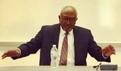 Robert Bullard sitting at a table talking enthusiastically with his arms in the air.