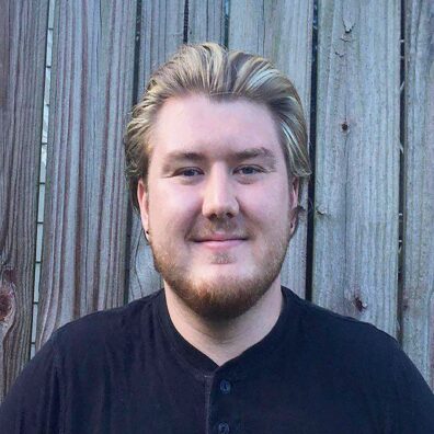 A front facing photo of Christian Maynard, from the shoulders up. They are looking into the camera and smiling.
