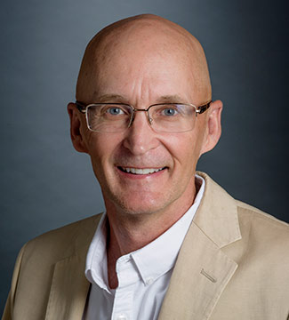 A front facing photo of Robin Perrin, from the shoulders up. He is looking into the camera and smiling.