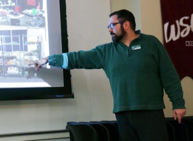 Joe is standing and pointing towards an image on a projected screen.