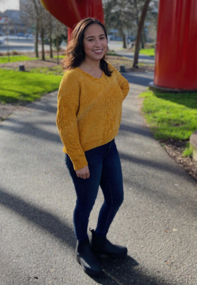 Marisa is standing and smiling towards the camera with one hand on her hip.