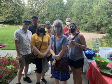 The group is bunched together and masked, with the Lawson garden flowers and trees seen behind them.