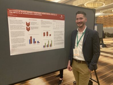 Caleb is standing next to his poster and smiling.