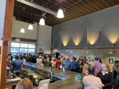 A distance view of the pub with many people around the bar and chatting.