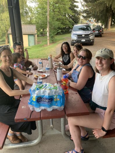 The people are seated around a picnic table outside and smiling towards the camera.