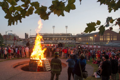 Crowd standing around bonfire with Martin Stadium and Hollingbery Fieldhouse in the background.