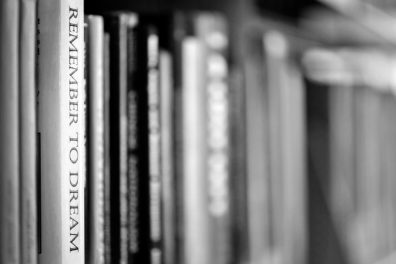 Dramatic photo of books in monotone with one book exposed and in focus saying, "Remember to dream"
