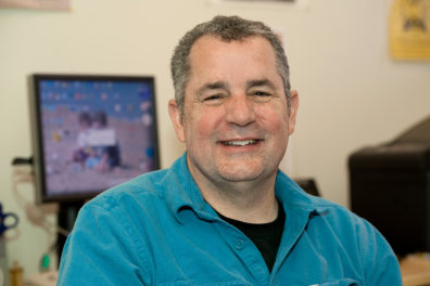 Patrick Carter posing in profile in front of a computer wearing a teal shirt.