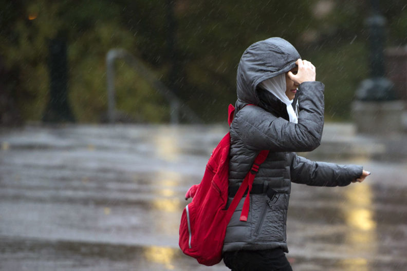 Female student in coat with hood up running in the rain.