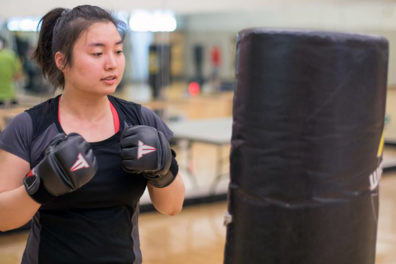 Gym goer with sparing gloves on prepares to hit a punching bag in the sweat the stress class