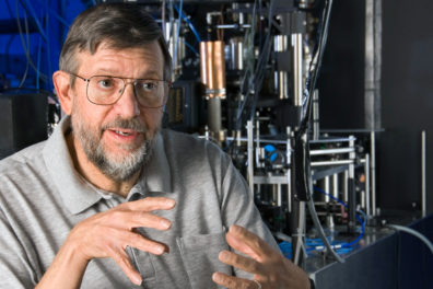 Nobel Laureate Dr. William Phillips in profile holding his hands as if he is explaining something.