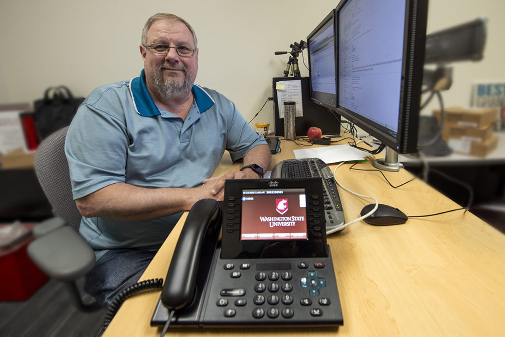 Phone with Cougar logo. Randy Cross at desk.