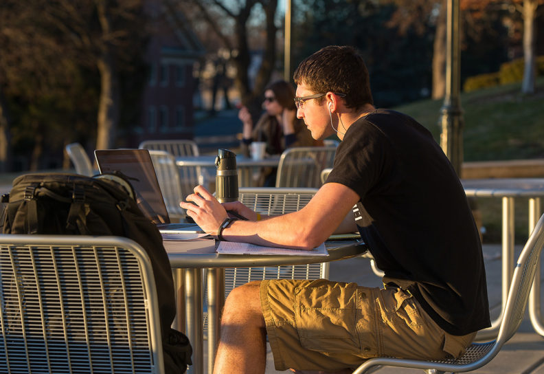 Student in shorts and short sleeve shirt sitting and studying outside.