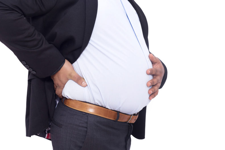 Overweight man with hand on stomach and back.