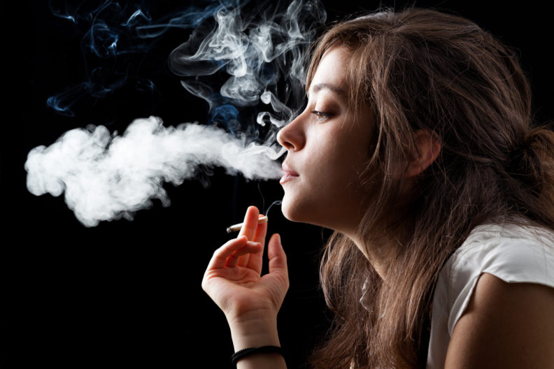 Woman with cigarette exhales billow of smoke.
