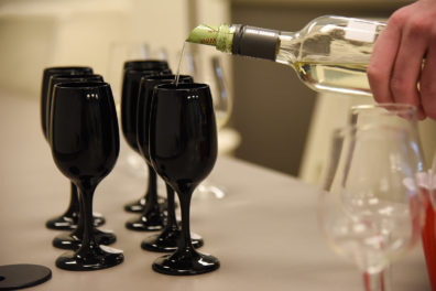 Wine is poured into one of several glasses lined up on a table.