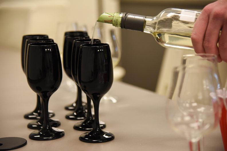 Wine is poured into one of several glasses lined up on a table.