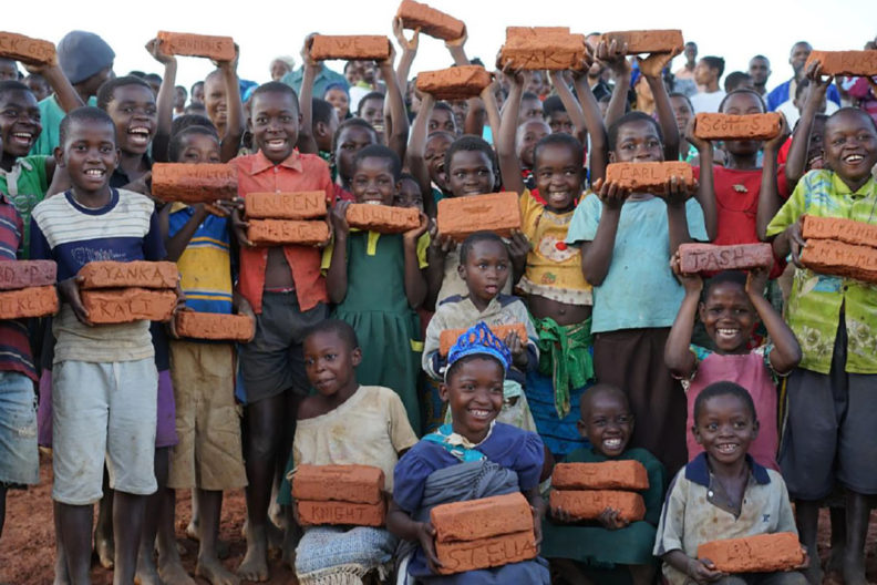 Large group of Malawi children holding bricks.