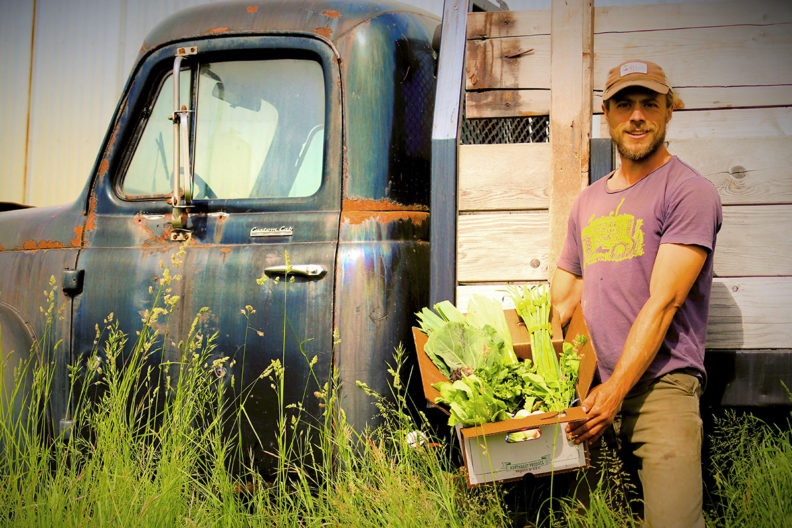 Olson holding a box of produce in front of an antique farm truck.