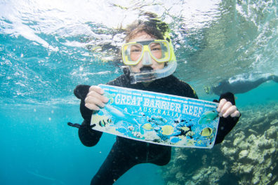 Johnson snorkeling and holding sign underwater that reads 'Great Barrier Reef'.