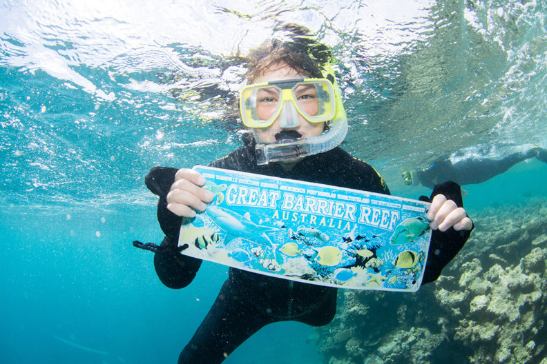 Johnson snorkeling and holding sign underwater that reads 'Great Barrier Reef'.