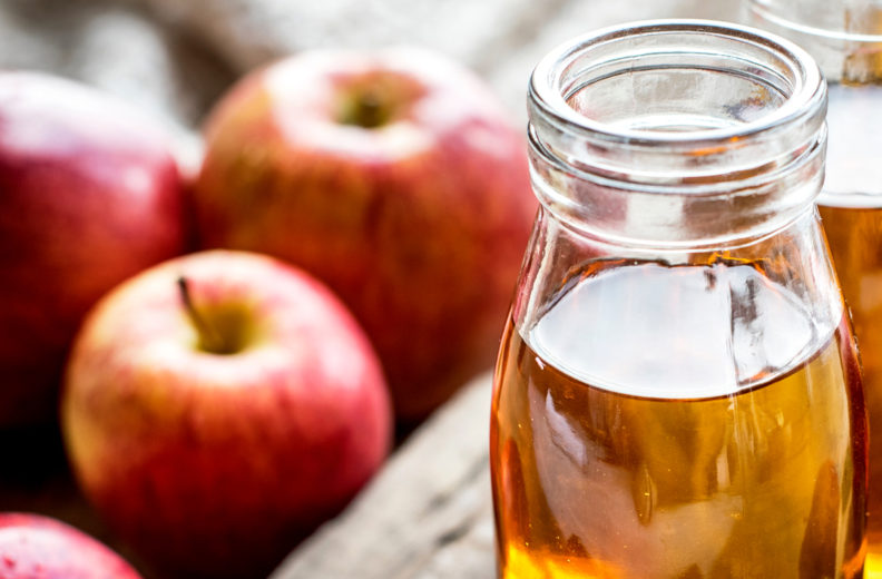 Apples and glass containers of cider.