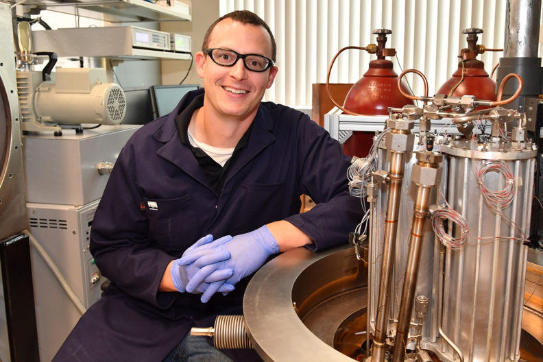Leachman in lab with tanks of gas beside him.