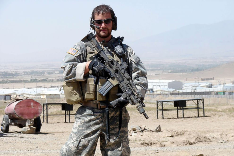 Shurer in Afghanistan in combat uniform and holding an machine gun.
