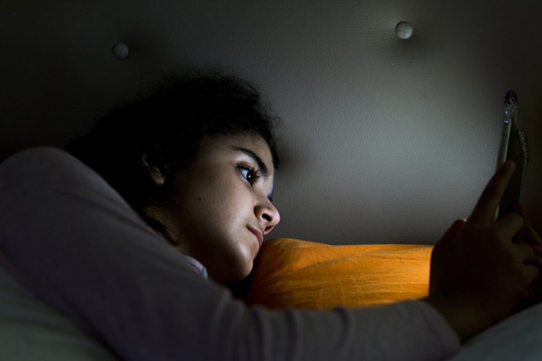 Teenage girl laying in bed looking at cell phone.