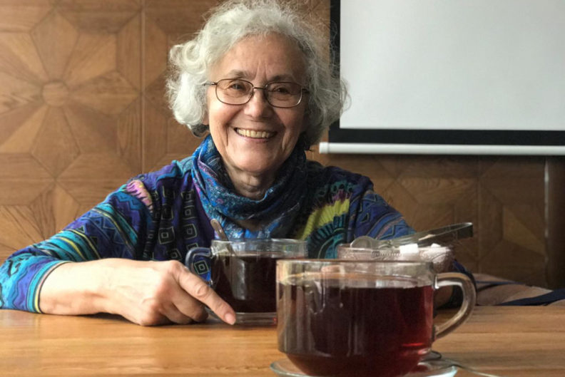 Tolmacheva sitting at table with cup of tea.