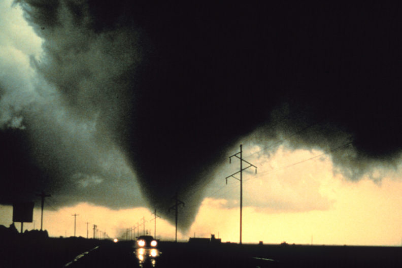 Large tornado in distance and car attempting to escape.