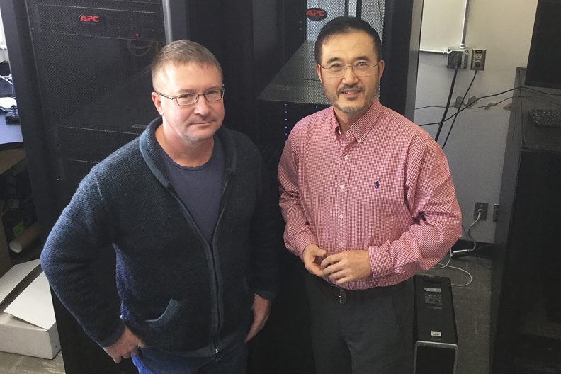 See and Zhang standing in front of large computer equipment.