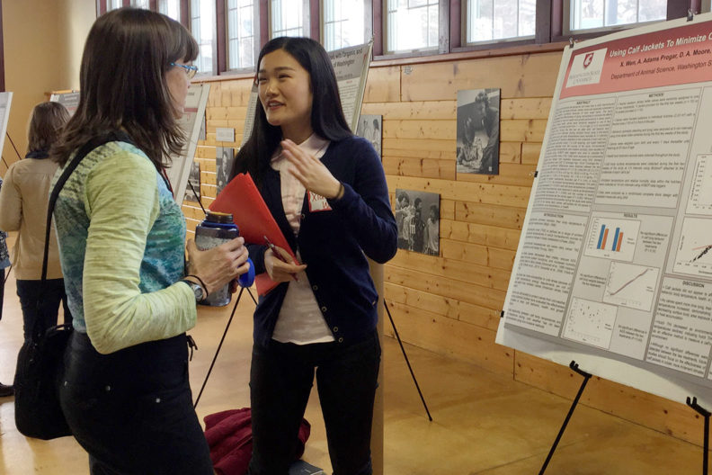 A presenter and attendee talk in front of poster display.
