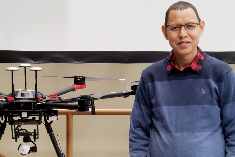 Karkee standing next to flying drone on table.