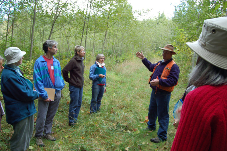 Forester talking to group of workshop participants in wooded area.