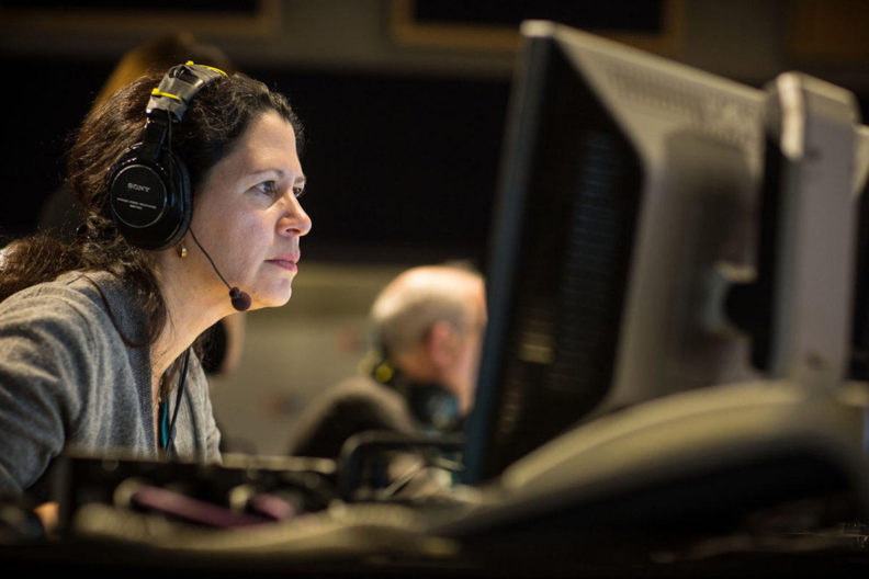 Block looking at computer monitor while wearing headphones and microphone.