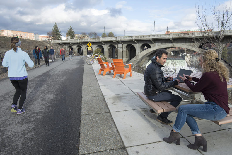 People running, walking and sitting on path by Spokane River.