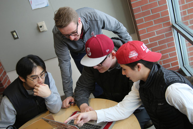 Students gathered around laptop discussing upcoming conference.