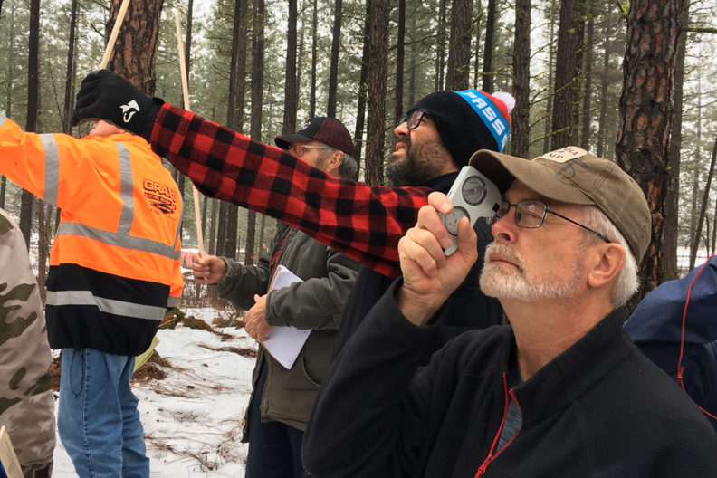 People in snowy forest measuring tree stand.