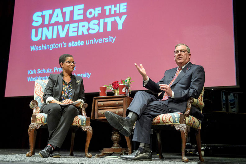 Donna Paul and Kirk Schulz sitting in chairs on stage during address.