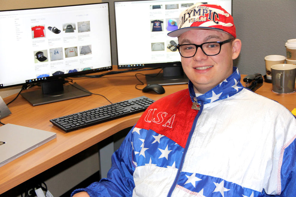 Dante Ludlow sitting next to a computer while wearing a 1996 Summer Olympics track suit.