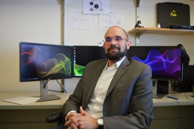 David Makin sitting in front of multiple computer monitors in office.