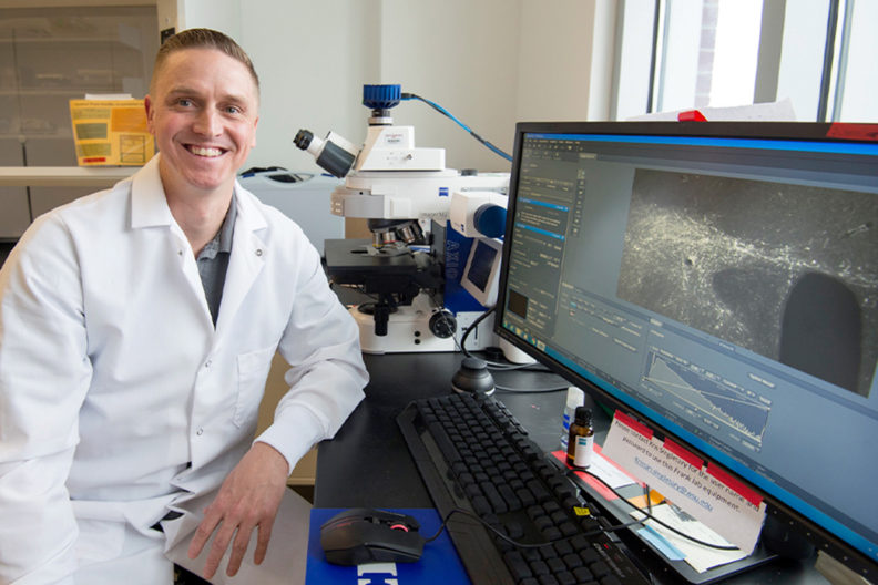 Willie Vanderheyden sitting next to a computer screen showing fluorescent microscopy images.