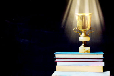 A golden trophy shines as it sits atop a pile of books.