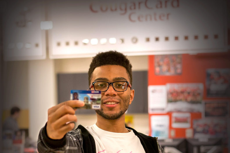 Student holding a CougarCard in front of the CougarCard Center.