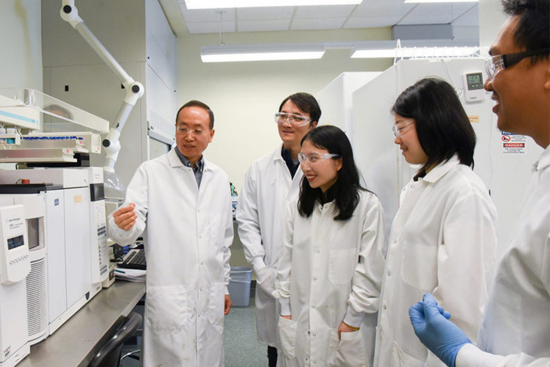 Lei and his team standing in a laboratory with lab coats.